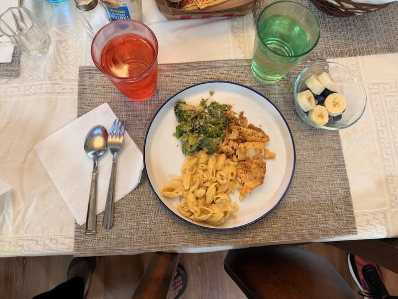 An individually plated meal: chicken, mac and cheese, broccoli, and fresh fruit